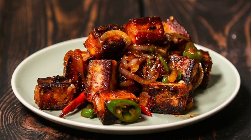 A plate of chili paneer with onions and peppers on a wooden table.