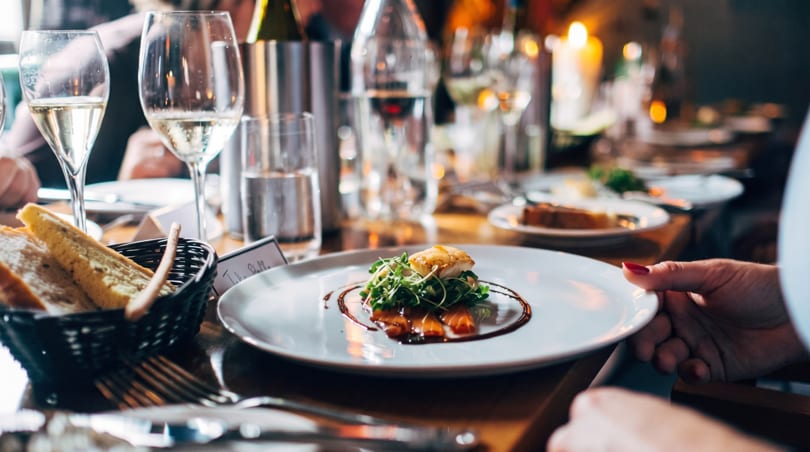 Elegant restaurant table with a plated appetizer, wine glasses, water, and a bread basket.
