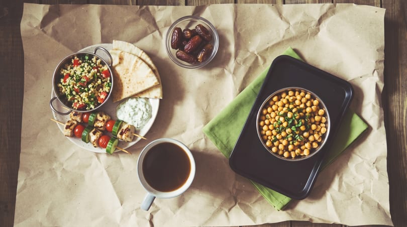 Overhead view of Middle Eastern meal with tabbouleh, skewers, chickpeas, dates, pita, and coffee.