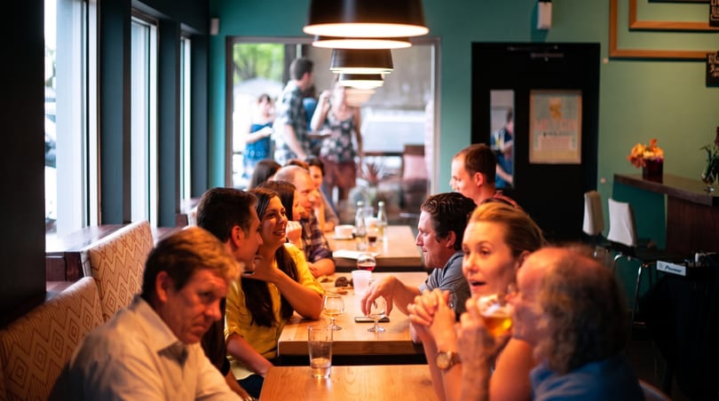 Customers enjoying drinks and conversation at wooden tables in a bustling restaurant.