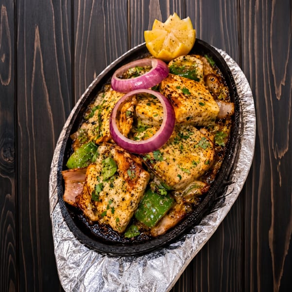 Sizzling platter of grilled paneer, green peppers, red onions, and a lemon wedge.