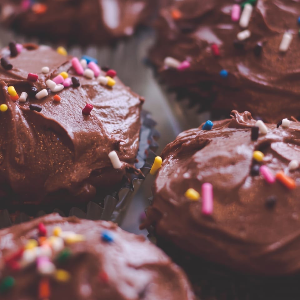 A tray of chocolate cupcakes with rich chocolate frosting and vibrant sprinkles.