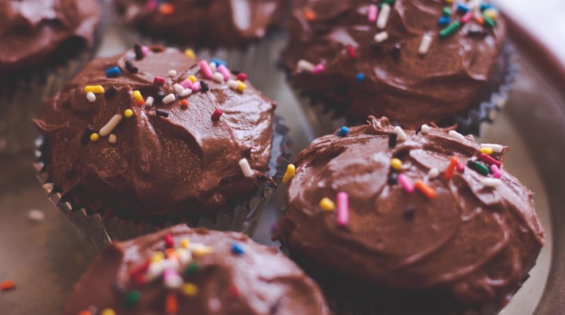 A tray of chocolate cupcakes with rich chocolate frosting and vibrant sprinkles.
