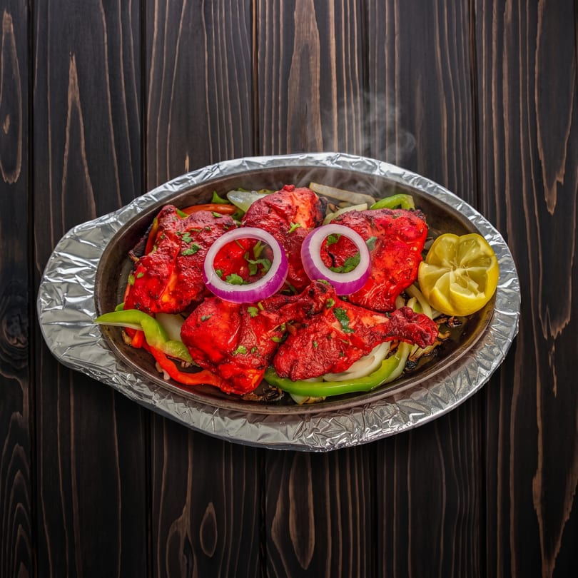 Sizzling Tandoori chicken with onions, bell peppers, and lemon on a hot platter.