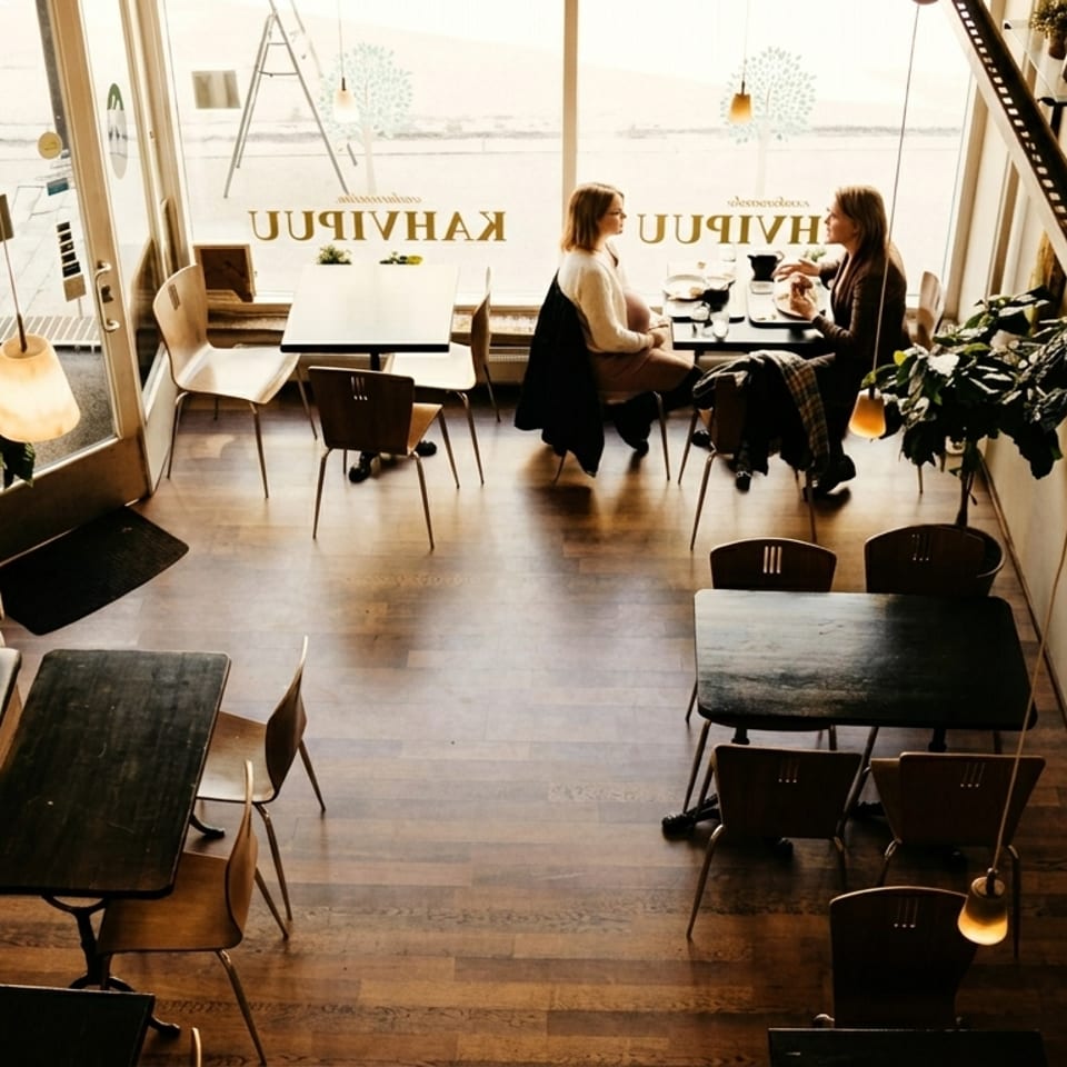 Overhead view of a cozy cafe with two women dining by a large window.