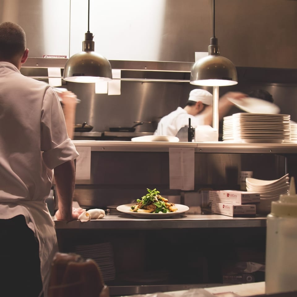 A chef overlooks a plated dish in a professional, bustling restaurant kitchen.